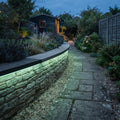 Green RGB neon flex following a curved garden wall beneath the coping and shining down