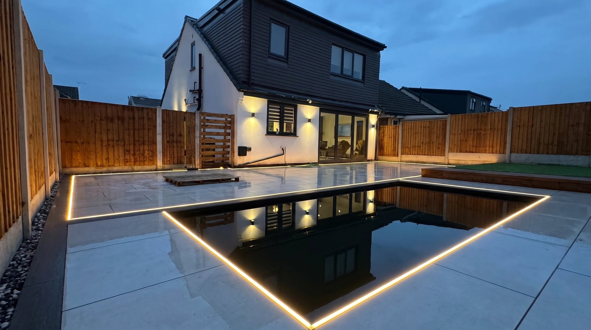 Warm white LED line running around a still reflecting pond set into a porcelain patio at dusk