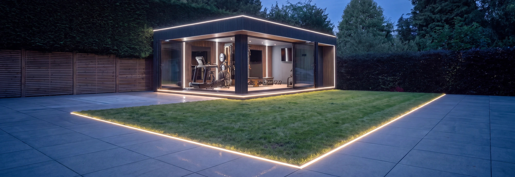 Lit garden gym room at dusk with warm white LED lines recessed around the lawn and paving