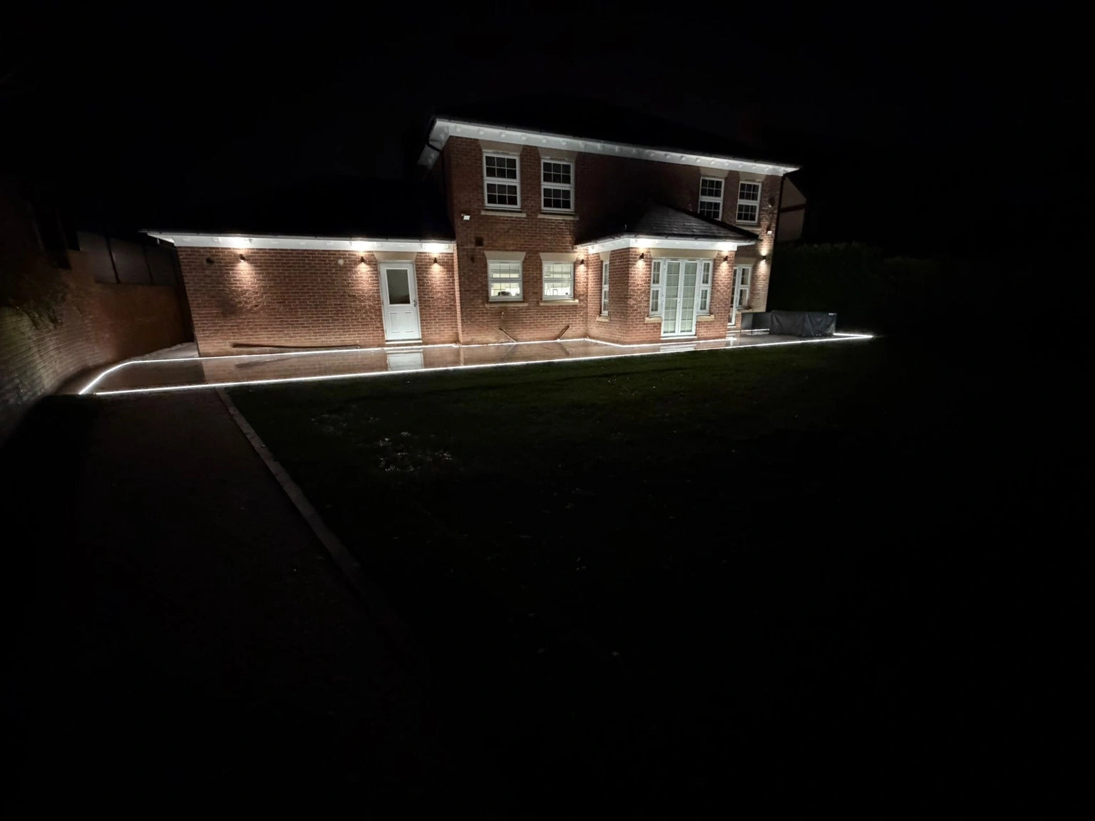 Wider distant view of the property at night with the perimeter ground-line strip and roofline lighting