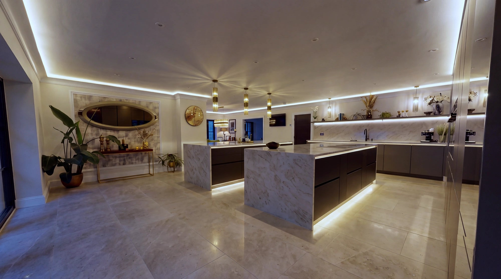 Open-plan kitchen at night with warm white COB LED cove lighting around the ceiling perimeter and light lines under both marble islands