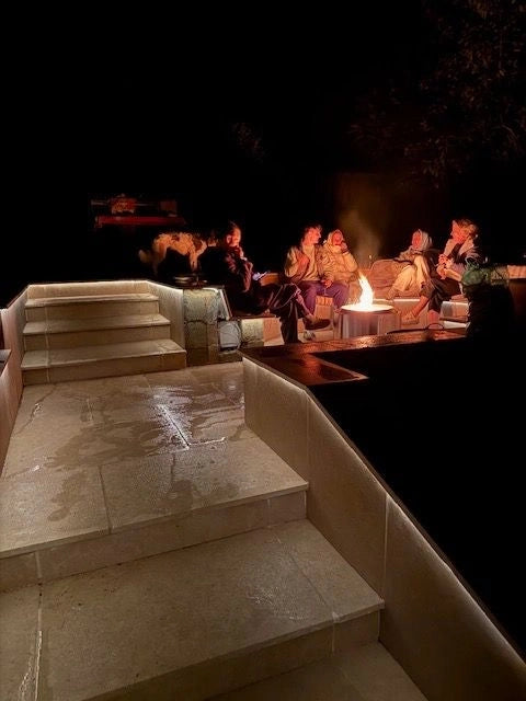 Sunken marble seating well at night with people gathered around the fire-pit, warm white perimeter glow