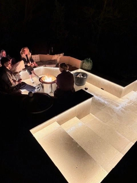Wider view of the marble seating well at night with people gathered around the fire-pit